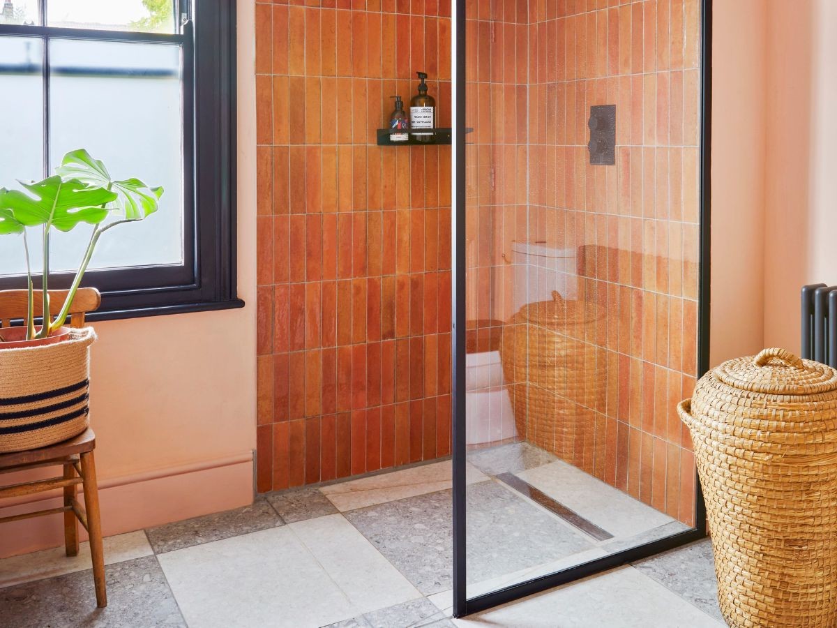 Douche zellige terracotta vertical posé sur sol gris clair, paroi verre noire et mur saumon avec fenêtre givré.